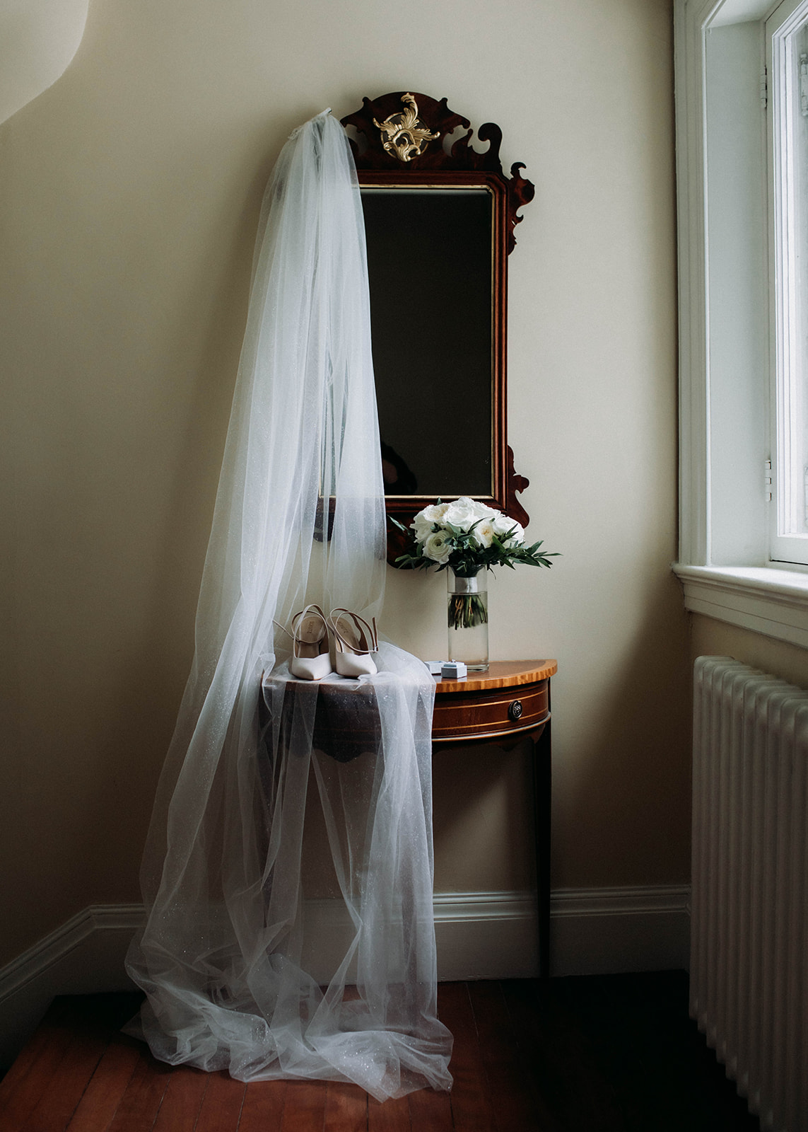 a wedding veil is hanging froma mirror and draped over a table with shoes and wedding bouquet sitting on top of it. This is a photo from a romantic coastal wedding in St. Andrews, New Brunswick photographed by Shannon-May