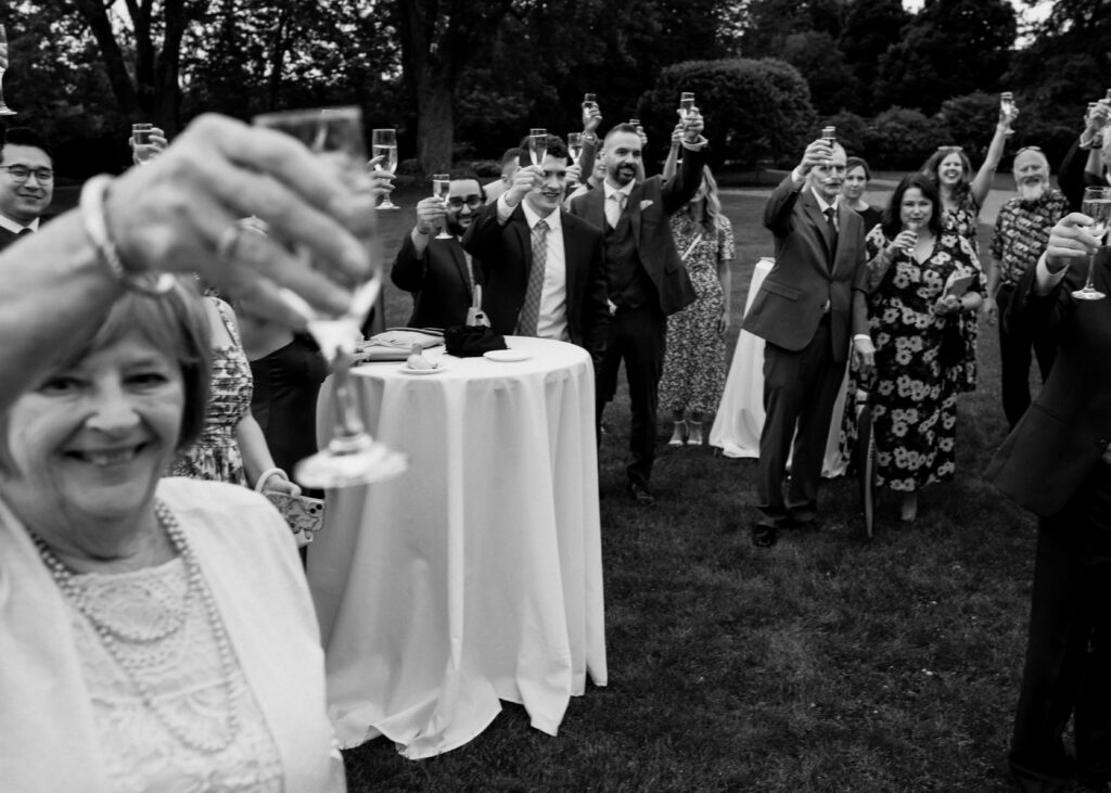 a black and white image of a group during a cocktail reception at kingsbrae garden. They are raising their glasses in the air in cheers. 