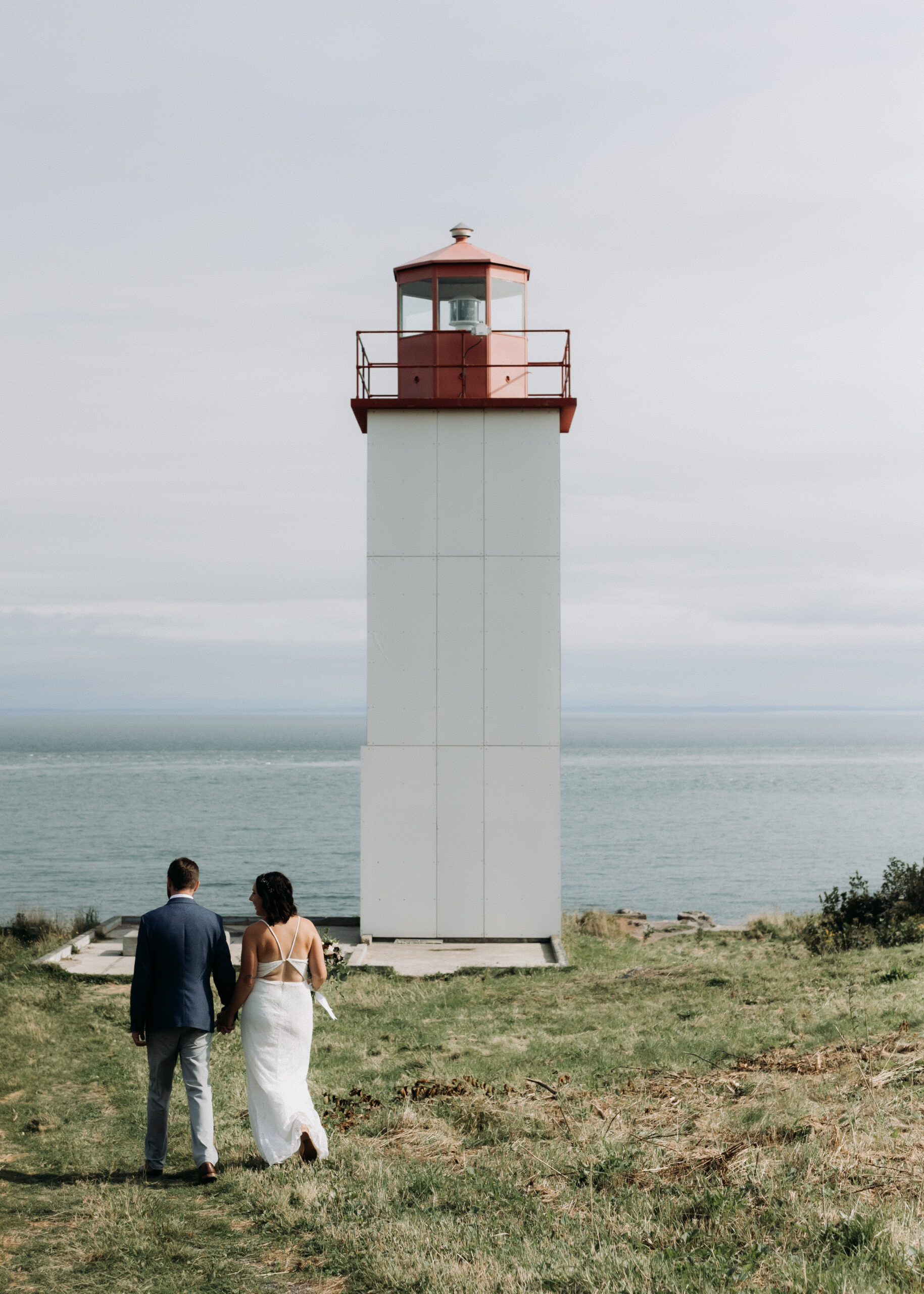 a couple has chosen to elope in New Brunswick. Together they walk hand in hand towards a lighthouse overlooking the ocean where they will exchange vows.